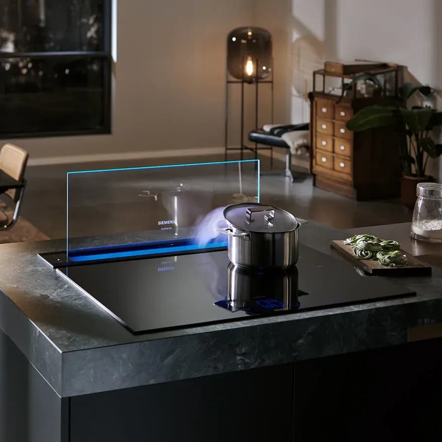 Moderne Kochstelle mit Glasabzugshaube, Topf auf der Fläche und stilvollem, minimalistischem Küchenambiente.